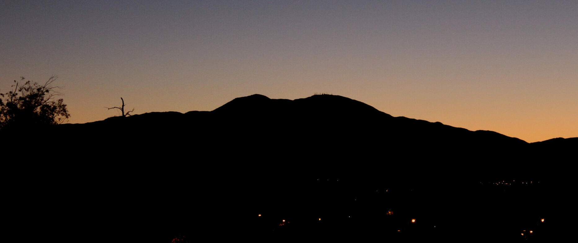 Saddleback Mountain, Orange County, California A silhouette of Saddleback Mountain against a pre-dawn sky, with a gradient from deep blue to orange. Distant city lights are scattered at the base of the mountain.